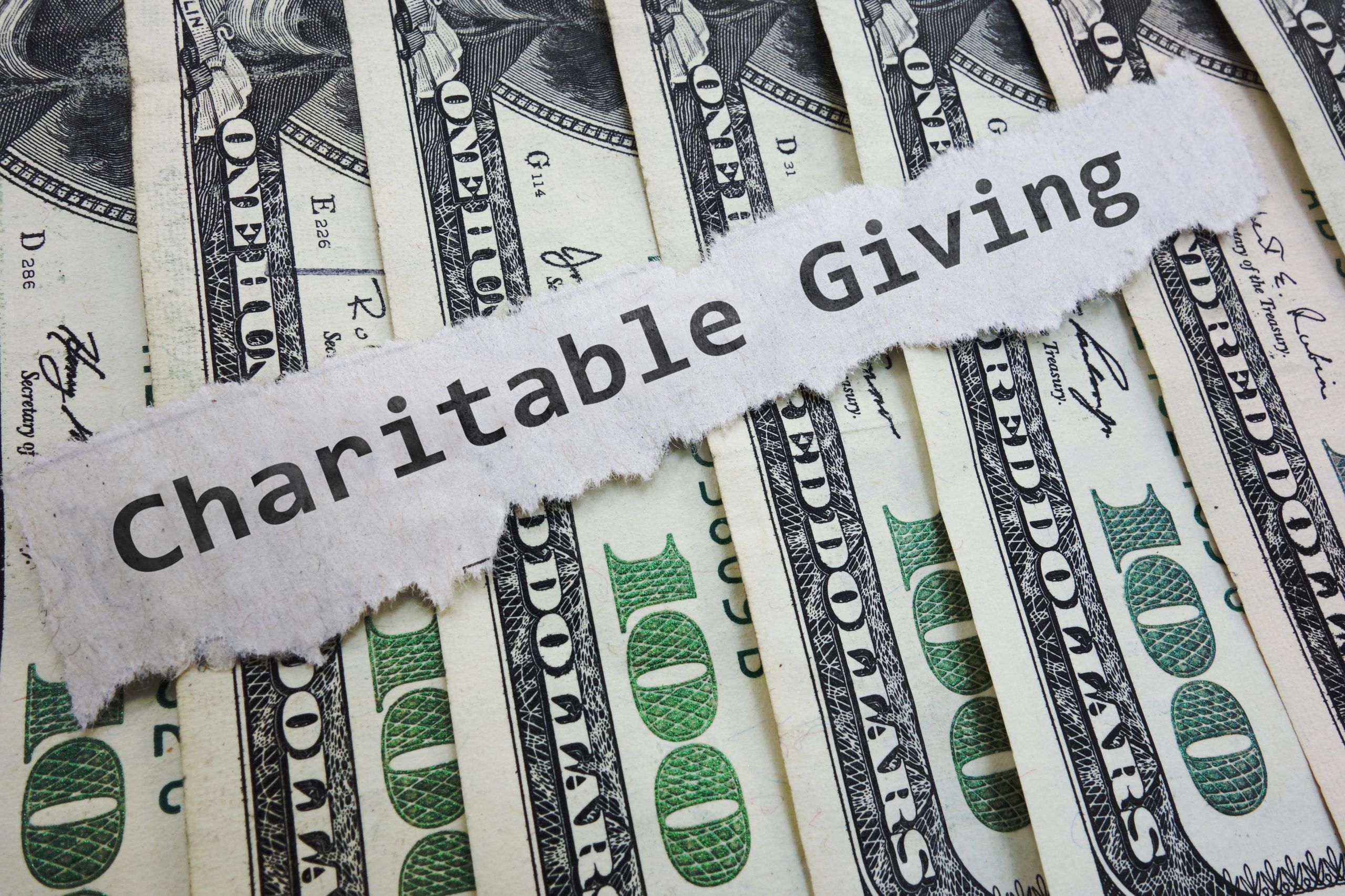 picture of 100 dollar bills and word charitable giving on a slip of paper